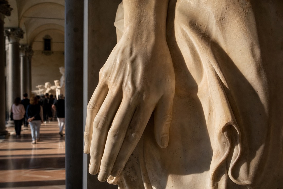 Close view of a carved marble hand with pronounced veins and tendons resting against stone drapery in a Florence museum