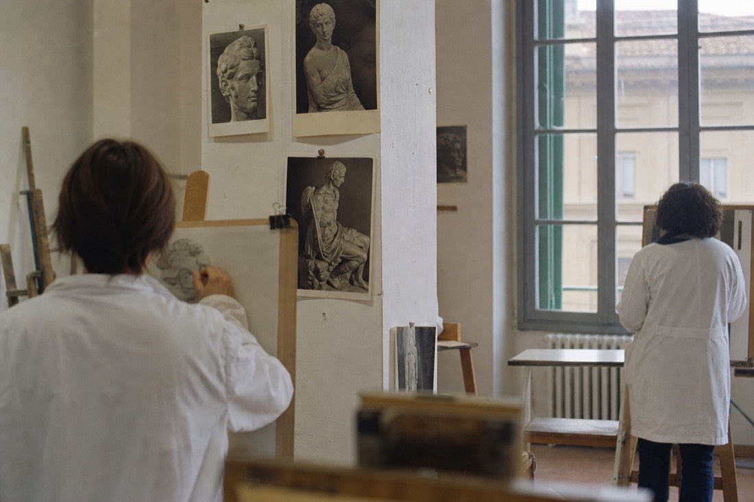 A bright school art classroom with reproductions of Renaissance sculptures pinned to the wall and empty wooden desks