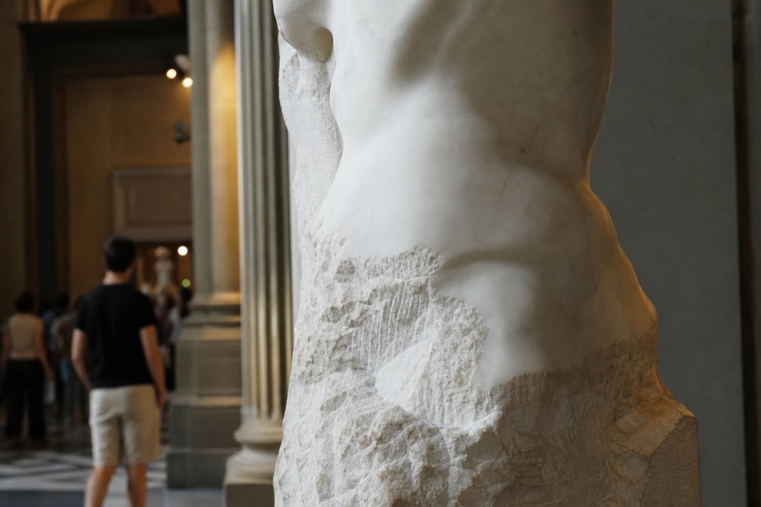 Close view of a partly carved marble torso showing smooth finished skin above and rough chisel marks below in a Florence gallery