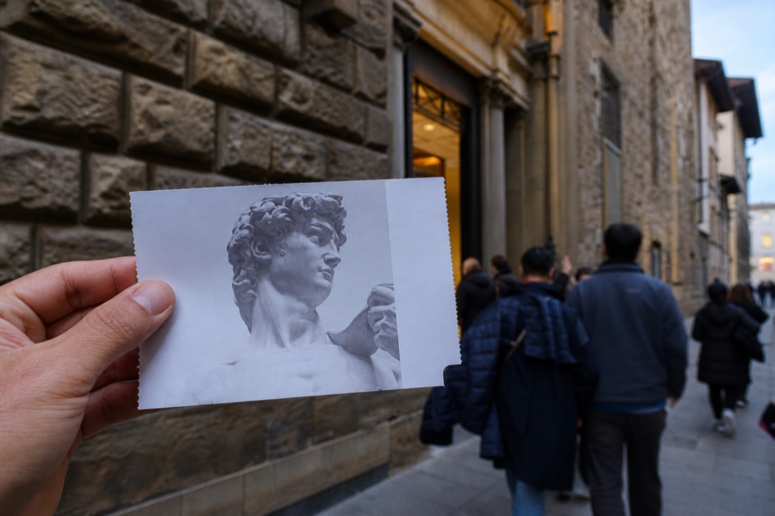 Close-up of a paper Accademia entry ticket held in front of the museum entrance sign on Via Ricasoli in Florence