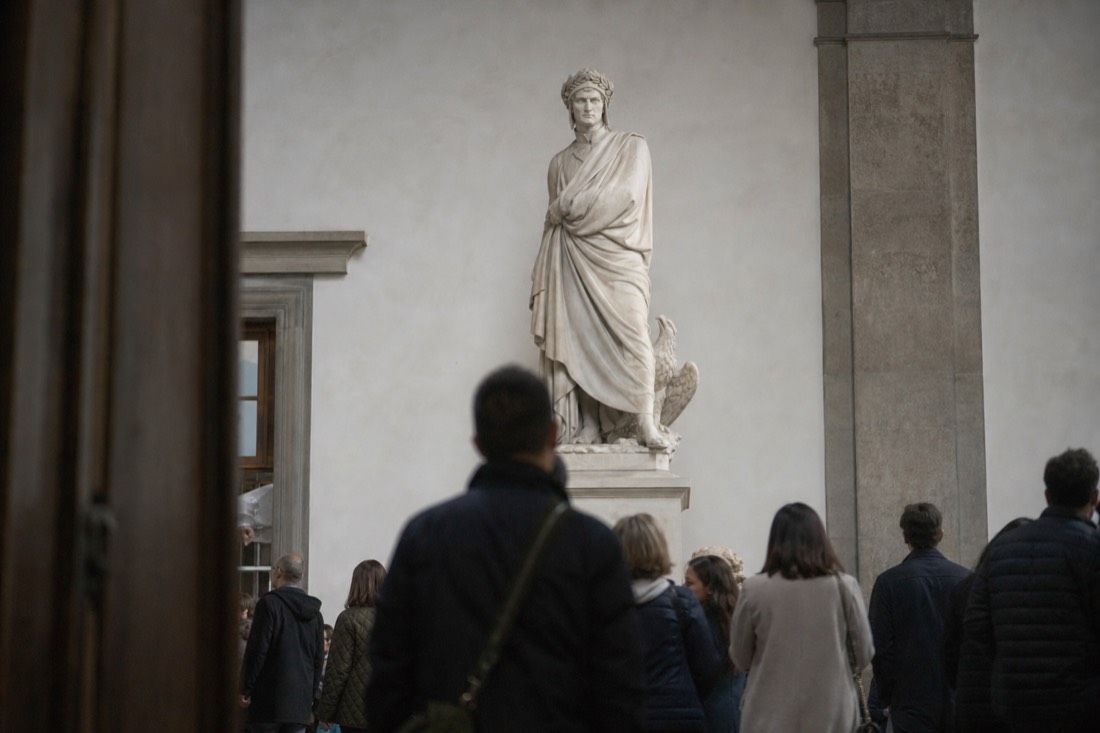 A monumental nude marble statue seen from the front in a museum hall, pale stone against a neutral wall