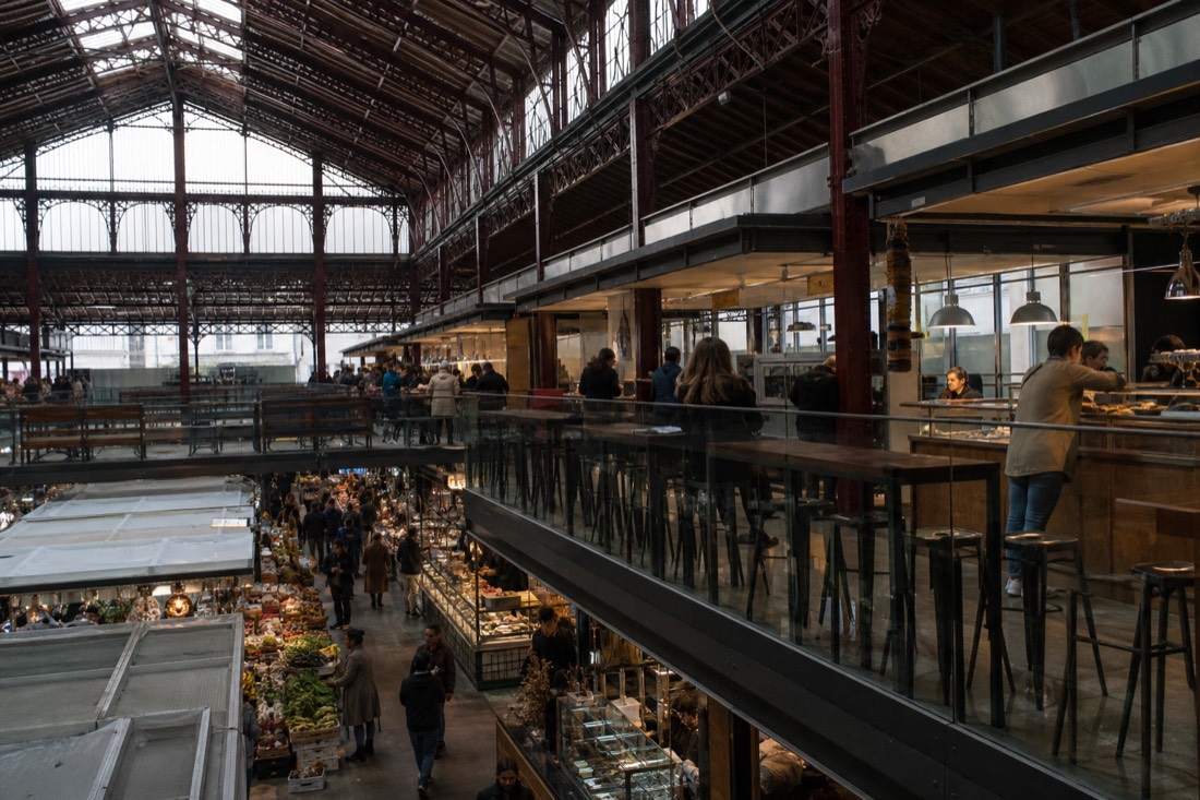 The tall iron and glass interior hall of the Mercato Centrale in Florence with market stalls below and food counters on the upper level