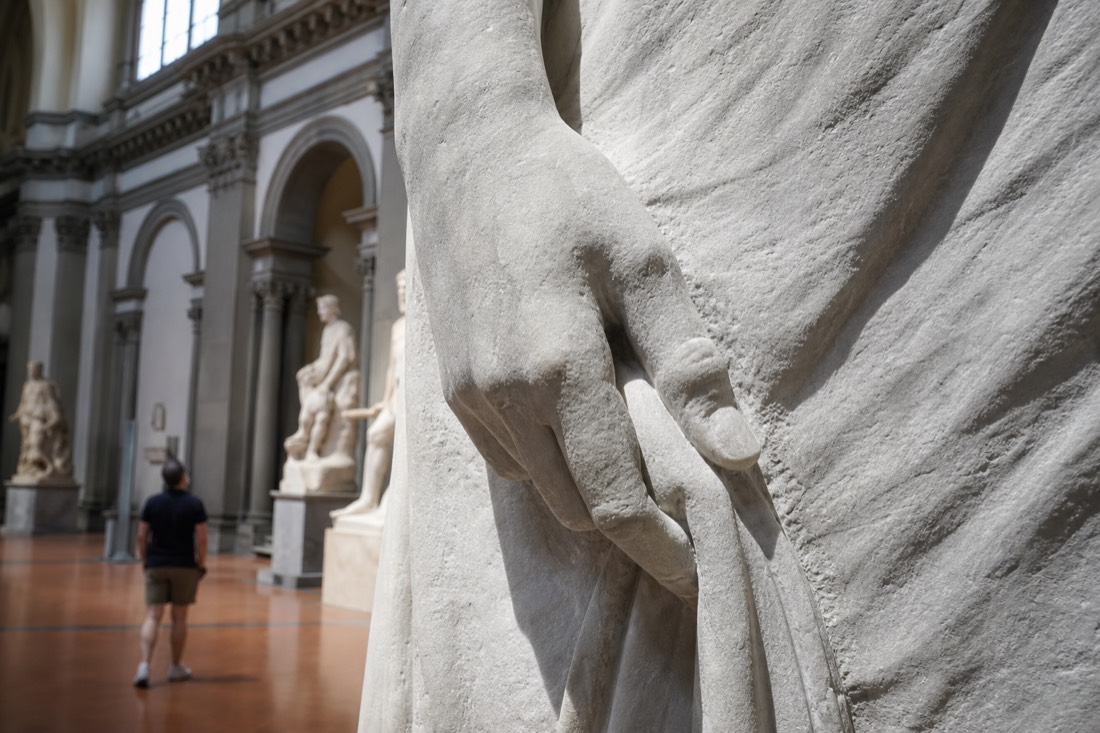 Close view of the chisel-marked marble surface and the tense right hand of Michelangelo's David in the Accademia Gallery