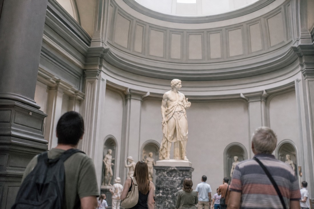 Visitors standing in the cool naturally lit tribune of the Accademia Gallery around the David sculpture on a summer day
