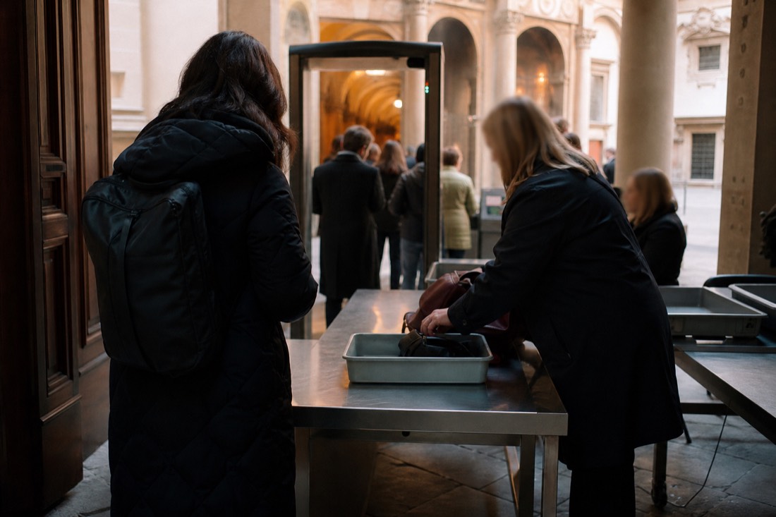 Close view of a security screening table at a Florence museum entrance with a metal detector arch and staff checking small bags