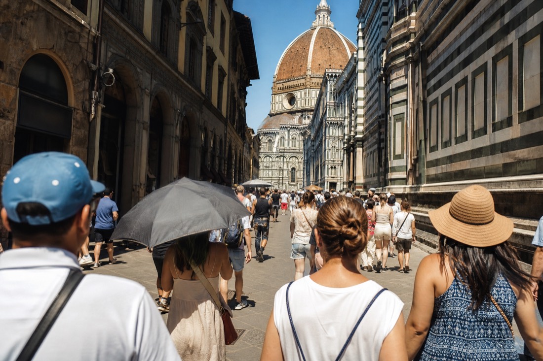 Crowded midday scene in central Florence with tourists filling a narrow street near the Duomo under bright sun