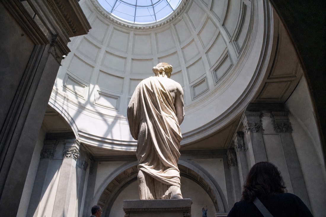 The marble figure of David seen from below under the bright skylit dome of the Accademia tribune in Florence