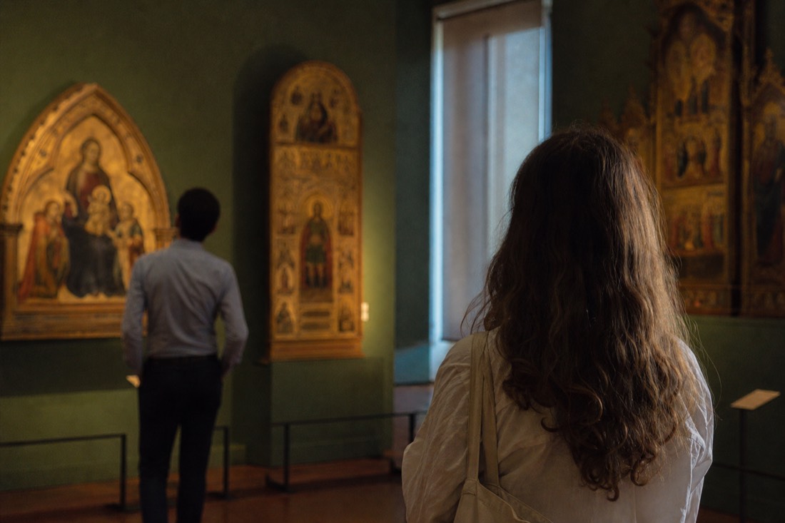 A quiet side room of a Florence museum with gold-ground altarpieces glowing on deep green walls