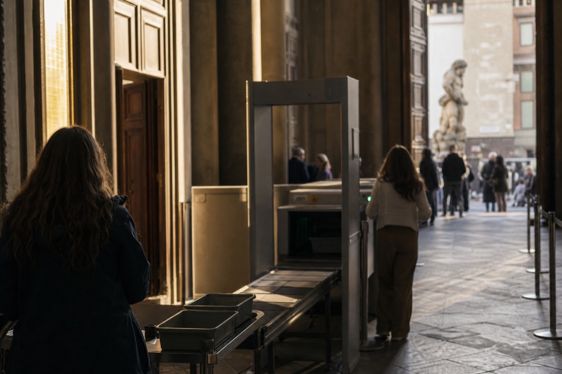 A security scanner and conveyor belt in the shadowed entrance hall of the Accademia Gallery in Florence