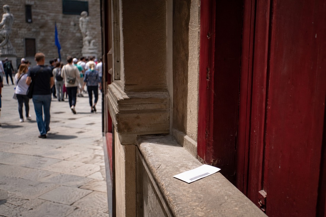 A printed timed entry ticket resting on a stone windowsill beside a deep red painted doorway in Florence