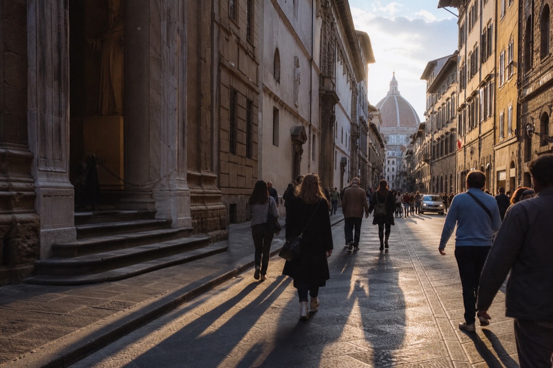 Long dawn shadows across Via Ricasoli with the Accademia Gallery doorway and the distant Duomo dome in Florence